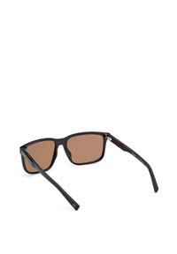 Czarne okulary przeciwsłoneczne z brązowymi soczewkami, kątowa konstrukcja i teksturowane czarne ramiona. Posiadają metaliczny akcent w pobliżu zawiasów.