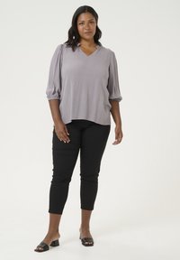 Blusa corta de manga corta en gris claro con escote en V y mangas fruncidas, combinada con pantalones negros hasta el tobillo y sandalias negras de tacón cuadrado.