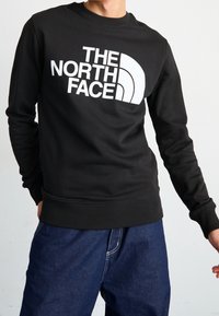 Sudadera negra con un gran logo blanco de "The North Face" en el pecho; cuello y puños de canalé; textura de tejido suave.