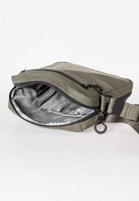Olijfgroene crossbody tas met een gladde buitenkant, ritsopening en lichtgrijze binnenkant. Bevat een verstelbare schouderband en een haak.