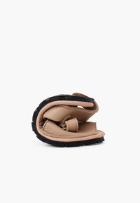 Sandale en cuir beige pliée avec une semelle en caoutchouc noir texturé. Présente deux lanières pour un maintien sécurisé. Design compact pour un rangement facile.