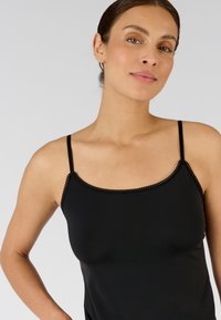 Camisole noire avec des fines bretelles et un délicat bord festonné le long de l'encolure. Fabriquée en un tissu lisse et extensible.
