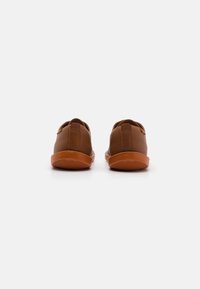 Scarpe in pelle marrone con suole in gomma, caratterizzate da un profilo basso e un design slip-on. Dettaglio di cucitura discreta sul retro.