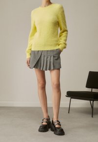 Jasnożółty, puszysty sweter w połączeniu z plisowaną spódnicą w czarno-białą kratę. Masywne czarne buty z ozdobnymi paskami.