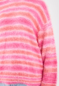 Pulover rayat roz și coral, cu o textură pufoasă și linii de lățimi variate. Design lejer, cu mâneci lungi.