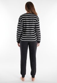 Schwarz-weißer gestreifter Langarmshirt mit einer lockeren Passform, kombiniert mit dunklen, weichen, tapered Jogginghosen, beide aus gemütlichem Stoff.