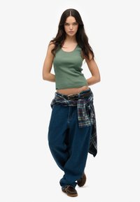 Groene geribbelde tanktop, losse blauwe spijkerbroek en een geruite blouse om de taille geknoopt. Bruine schoenen met gestructureerde zolen maken de outfit compleet.
