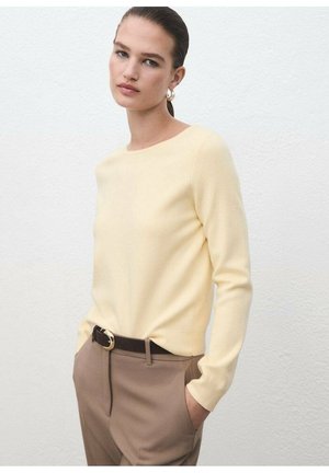 Suéter amarillo de manga larga con cuello redondo, combinado con pantalones marrones y un cinturón que cuenta con una hebilla en tono dorado. Textura suave.