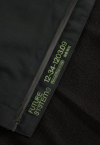 Crni materijal s dijelom munje na kojem se nalazi zeleni tekst: "FUTURE SYSTEMs 12-34-1203.09 Reboot Programme" i mali japanski znakovi.