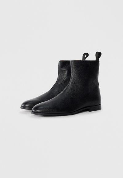 Botas de tobillo de cuero negro con un acabado texturizado, diseño elegante, punta redondeada y lengüetas en el cuello. Suela de goma plana.