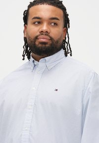 Vaaleansininen nappipaita, jossa on kuvioitu pinta, kaulus ja pieni logo rinnassa. Paidassa on valkoiset napit ja rento istuvuus.