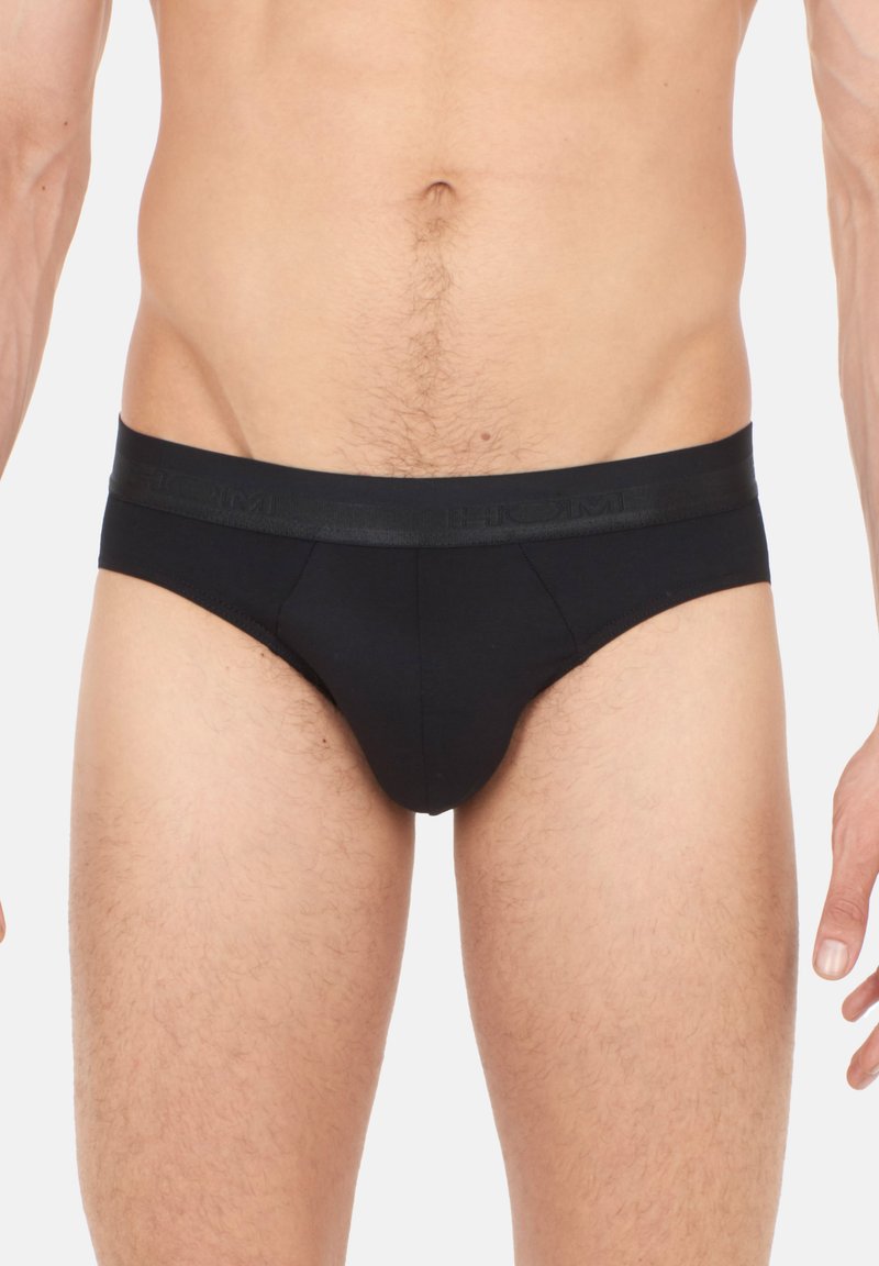 Schwarze Baumwollunterwäsche mit einem Satinhüftbund, der geprägtes Branding aufweist. Sie sind für Komfort und eine enge Passform gestaltet und präsentieren eine glatte Textur.