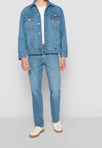 Vaate denimjakku vaaleansinisellä värillä, jossa on napit, kaksi etutaskua rinnan kohdalla ja rento istuvuus. Se on yhdistetty vaaleansinihin farkkuihin ja valkoisiin lenkkareihin.