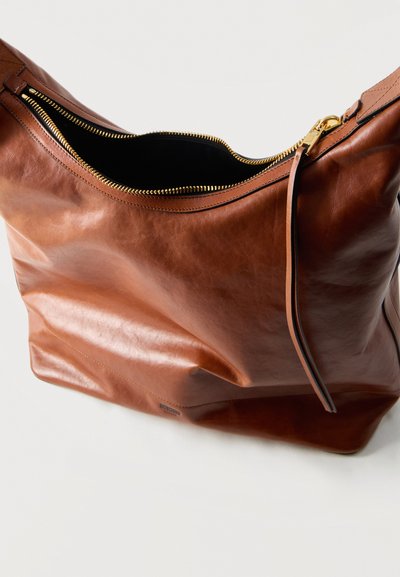 Sac à main en cuir marron avec fermeture éclair dorée partiellement ouverte, révélant un intérieur noir, et une fine languette en cuir sur un fond uni.