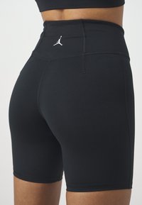 Gros plan d'une personne portant un short de sport noir taille haute avec un logo Jumpman blanc sur la ceinture arrière.