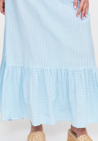 Jasnoniebieska, w paski maxi sukienka z falbanksą u dołu. Wykonana z miękkiego materiału, ma cienkie pionowe białe paski i zwiewny krój.