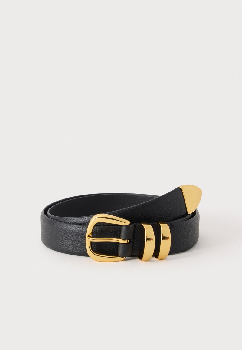 Ceinture en cuir noire roulée avec boucle en métal doré, deux passants et une pointe dorée sur un fond clair uni.