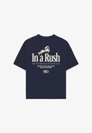Námořnicky modré tričko s krémovým nápisem "In a Rush International", grafikou skákajícího koně a menším textem "Modern Yuppies Worldwide Berlin Avantgarde."