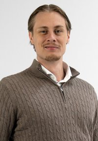 Bruin gebreid sweater met een kabelpatroon, hoge kraag en rits. Draagt over een wit overhemd met knopen.