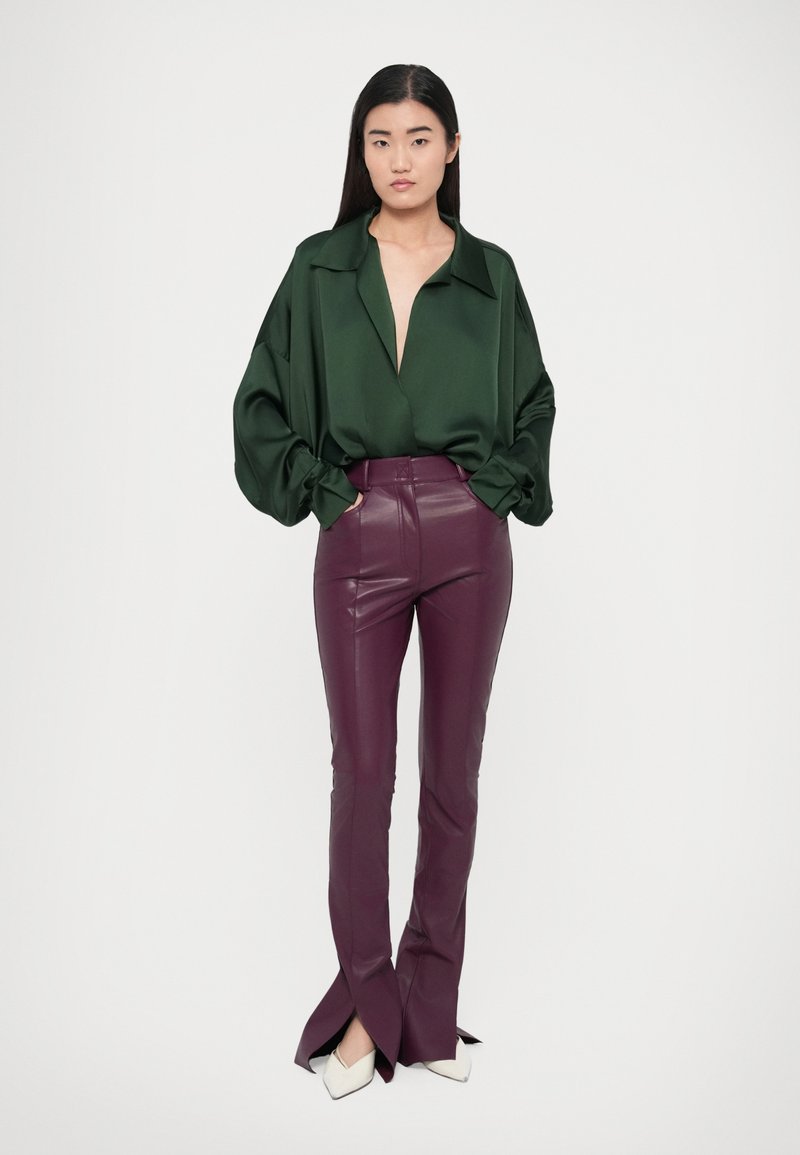 Green satin blouse with a deep V-neck and oversized sleeves, paired with high-waisted, plum leather flared pants with split hems. White pointed shoes.