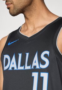 Schwarzes Basketballtrikot mit dem Schriftzug "DALLAS" in Hellblau, darunter die Nummer "11". V-Ausschnitt mit grauen Akzenten.