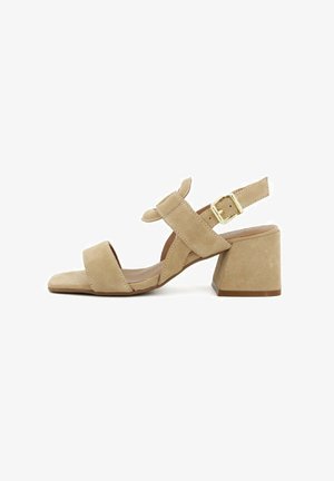 Sandali in suede beige con tacco a blocco, due fasce anteriori e una fascia alla caviglia. Presentano una fibbia dorata per la chiusura e un design a punta quadrata.