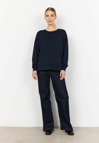 Navy blue oversized sweatshirt made of soft fabric, paired with high-waisted dark denim flared pants. Simple design with subtle stitching accents.