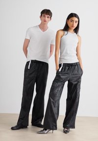Black cargo-style pants with a shiny texture and side pockets, paired with a white v-neck shirt and a gray tank top.