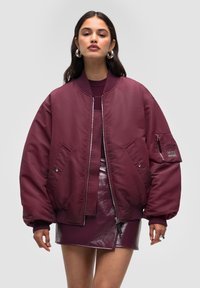 Vinröd bomberjacka med en glansig, slät yta, dragkedjefickor och ribbade muddar. Bärs över en matchande blank minikjol.