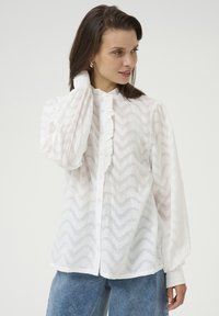 Witte blouse met knopen, voorzien van een textuurpatroon in zigzag, een gerimpelde kraag en volumineuze mouwen met elastische manchetten. Denim-look onderkleding.