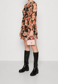 Svart blommig klänning med persikorosor, volangärmar och flerskiktad kjol. Ett par knähöga svarta läderstövlar och en liten rosa handväska.