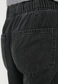 Μαύρο παντελόνι τζιν με ελαστική ζώνη μέσης, διαθέτει δύο πίσω τσέπες με ευθείες άκρες, ορατή ραφή και υφή υφάσματος.