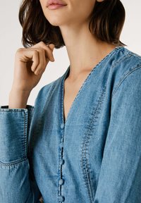 Džinsu krekls ar V veida kaklu, pogu slēgšanu ar teksturētām apaļām pogām un strukturētām piedurknēm ar izstrādātu stitchingu. Gaiši zila krāsa.