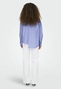 Camicia oversize a righe blu con design a spacco, abbinata a pantaloni bianchi a gamba larga. Caratterizzata da maniche lunghe e vestibilità comoda.