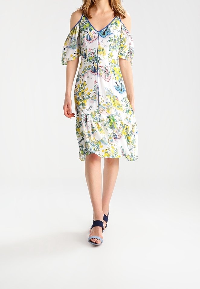 Bloemige jurk met off-the-shoulder mouwen, v-hals en verzamelde zoom. Multicolor bloemenpatroon op een witte stof. Gemaakt met marineblauwe en lichtblauwe sandalen.