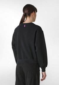 Svart sweatshirt med rundad halsringning, nedhasade axlar, ribbad muddar och nederkant. Har en liten rosa etikett vid bakre halsringningen.