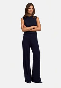 Marineblauw jumpsuit met een mouwloos, hoog halsontwerp, gemaakt van zachte stof. Voorzien van wijde broekspijpen en een getailleerd lijfje voor comfort.