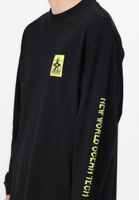 Black long-sleeve t-shirt made of cotton. Features a neon green logo on the chest and text along the left sleeve in the same color.