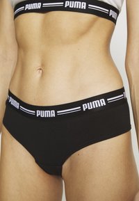 Crne pamučne gaćice s širokim elastičnim pojasom na kojem je napisano "PUMA" bijelim slovima. Glatka tekstura i prilagođen dizajn.