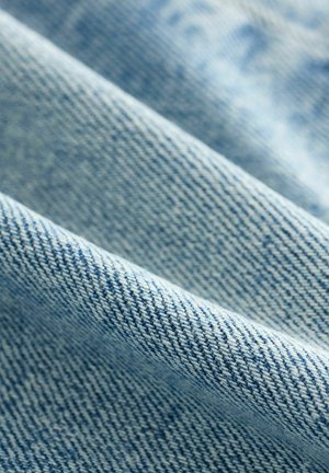 Ljusblå denimtyg med en texturerad väv, som visar en twillmönster och mjuk yta. Tyget verkar något skrynkligt.