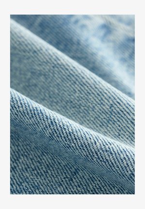 Ljusblå denimtyg med en texturerad väv, som visar en twillmönster och mjuk yta. Tyget verkar något skrynkligt.