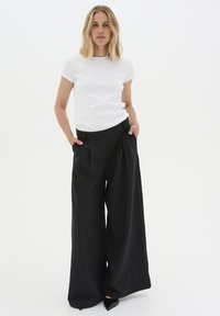 White ribbed short-sleeve top with logo, paired with high-waisted black wide-leg trousers. Trousers feature front pleats and pockets.