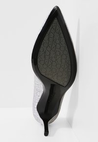 Talons hauts gris texturé avec un bout pointu et une semelle noire brillante présentant une traction à motifs. Logo de la marque visible sur la semelle intérieure.