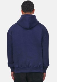 Hoodie bleu marine avec une capuche spacieuse, des manches longues et des poignets et ourlet côtelés. Tissu doux avec une texture lisse et un design minimaliste.
