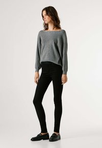Suéter gris de punto con un escote amplio y mangas abullonadas, combinado con jeans negros ajustados y zapatos de slip-on negros.
