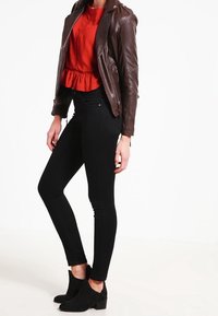 Brun læder bikerjakke, rød peplum top, sorte skinny jeans og sorte ankelstøvler. Glatte teksturer og tætsiddende design hele vejen igennem.
