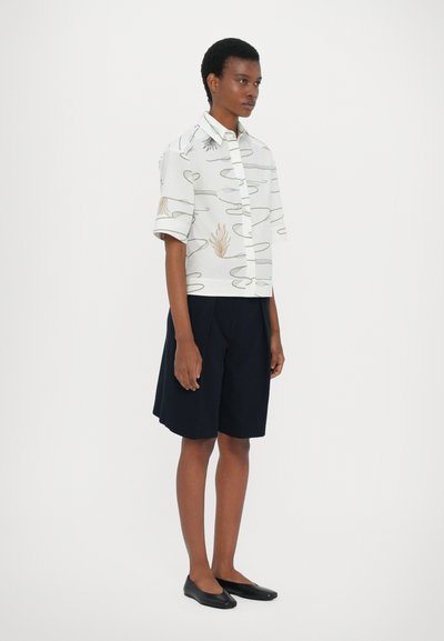 Short-sleeve, white blouse with abstract line and flame patterns; paired with navy shorts. Smooth fabric, relaxed fit, and simple button closure.