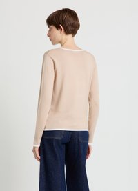 Beige long-sleeve sweater with a round white collar and textured fabric, paired with dark blue wide-leg jeans.