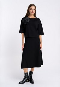 Czarny dwuczęściowy strój składający się z krótkiego topu z szerokimi rękawami oraz długiej spódnicy. Udekorowany kwiatowym detalem na ramieniu.