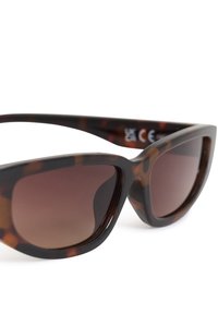 Lunettes de soleil œil de chat écaille de tortue marron avec des verres dégradés foncés et des montures légèrement épaisses.